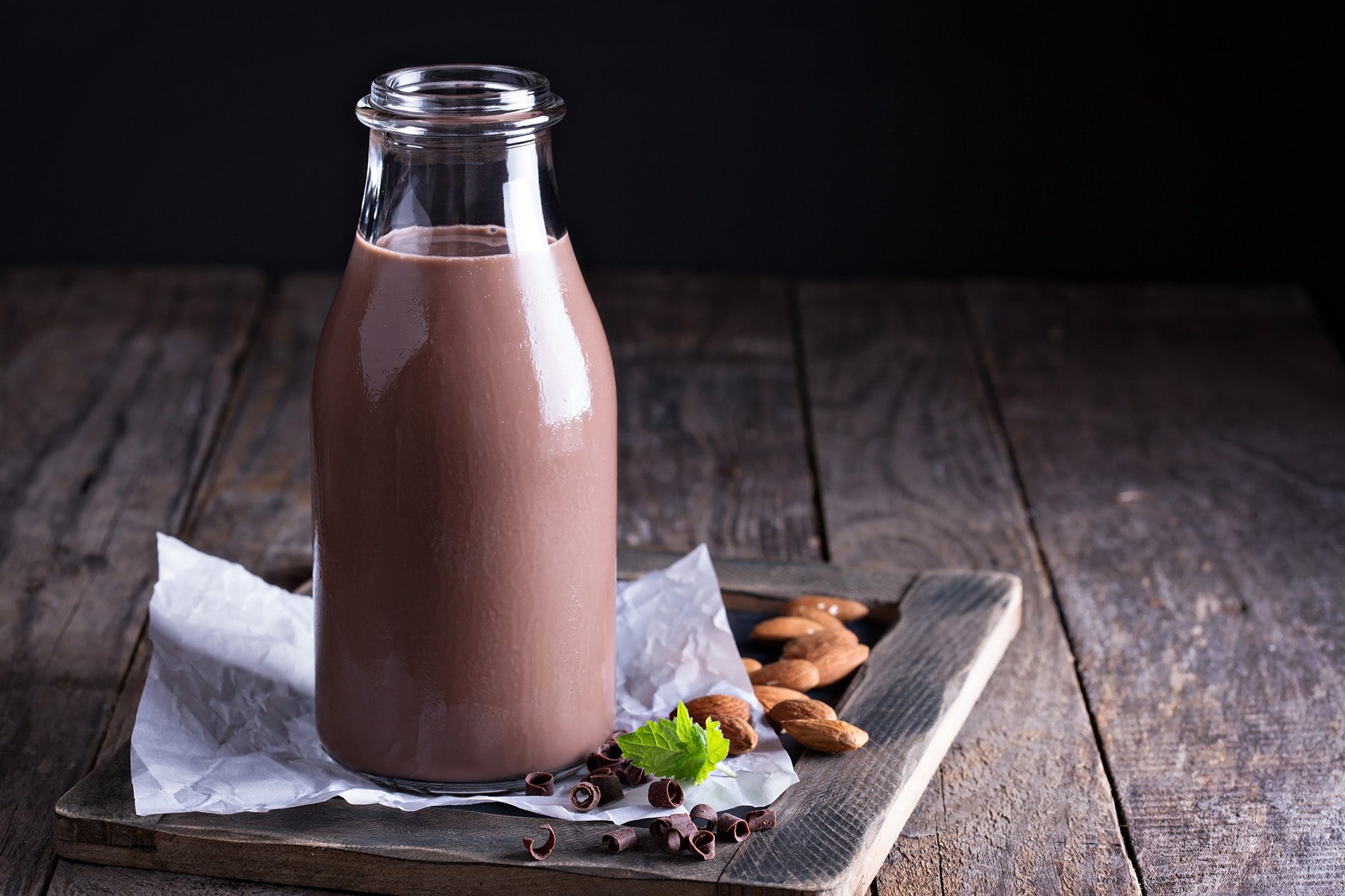 chocolate almond milk in a glass next to almonds on a wooden table